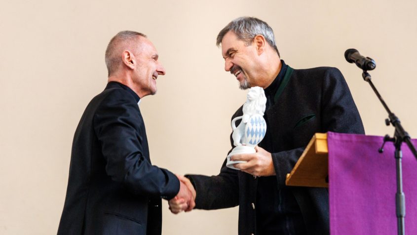 Ministerpräsident Dr. Markus Söder (rechts) übergibt Kirchenrat Dieter Breit (links) bei dessen Verabschiedung ein Geschenk.