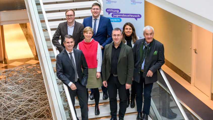 Gruppenbild unter anderem mit Europaminister Eric Beißwenger (links), der Geschäftsführung der Stiftung zur Förderung des Internationalen Jugendaustausches in Bayern, Mirjam Eisele (3. von links) und Wolfgang Schwarzenberger (3. von rechts), dem Präsidenten des Bayerischen Jugendrings, Philipp Seitz (2. von links), sowie dem Beauftragten der Bayerischen Staatsregierung für jüdisches Leben und gegen Antisemitismus, für Erinnerungsarbeit und geschichtliches Erbe, Staatsminister a.D. Dr. Ludwig Spaenle (rechts).