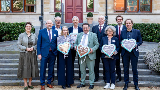 Zehn Personen stehen vor der Bayerischen Vertretung in Br&uuml;ssel und halten wei&szlig;-blaue Lebkuchenherzen in der Hand.